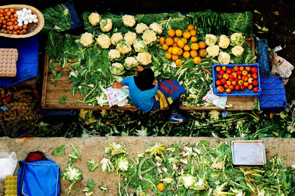Young vendor at a vibrant market stall in İzmir, Türkiye, displaying fresh produce from above.